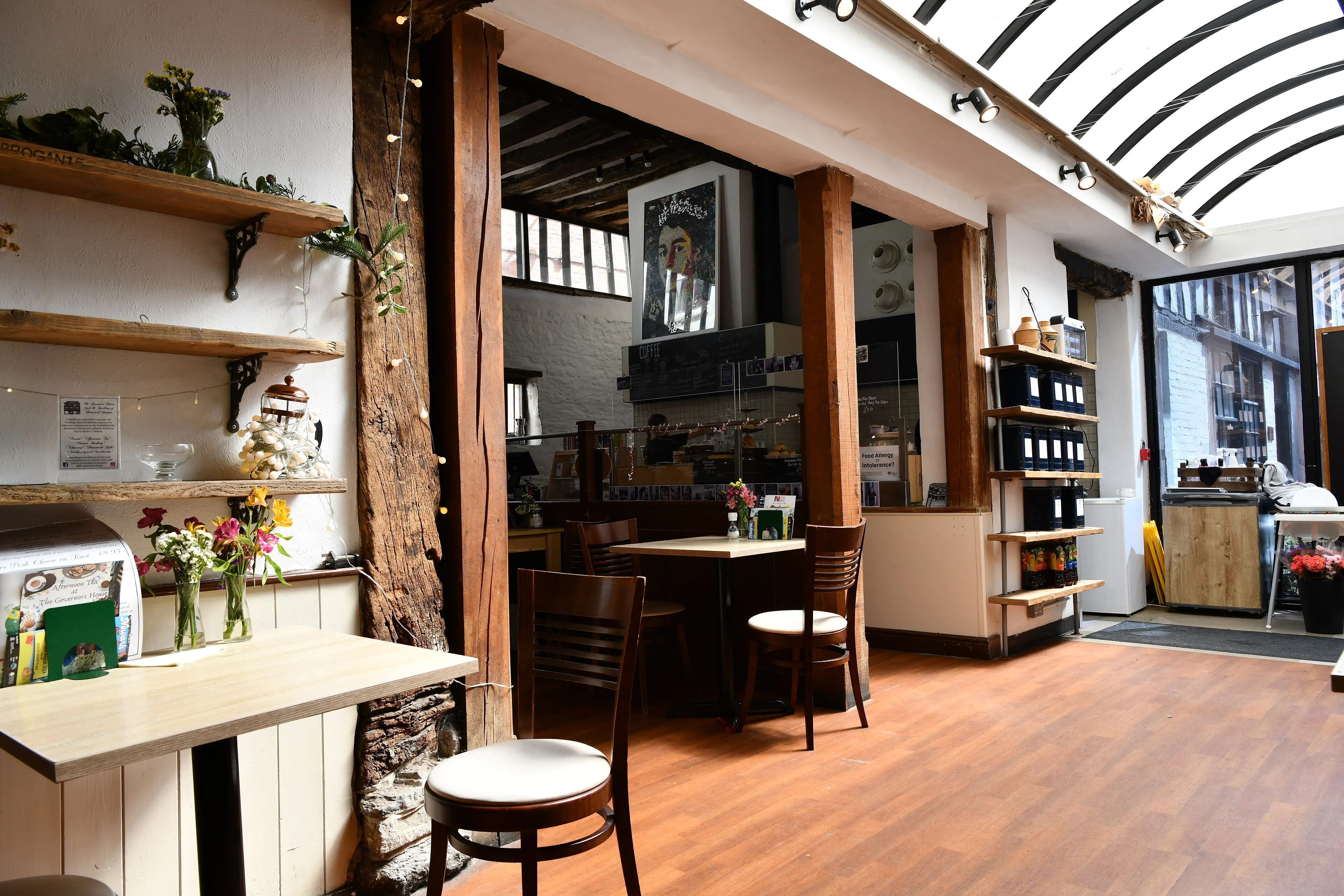 Inside a small coffee shop with wooden tables and plants on the shelves