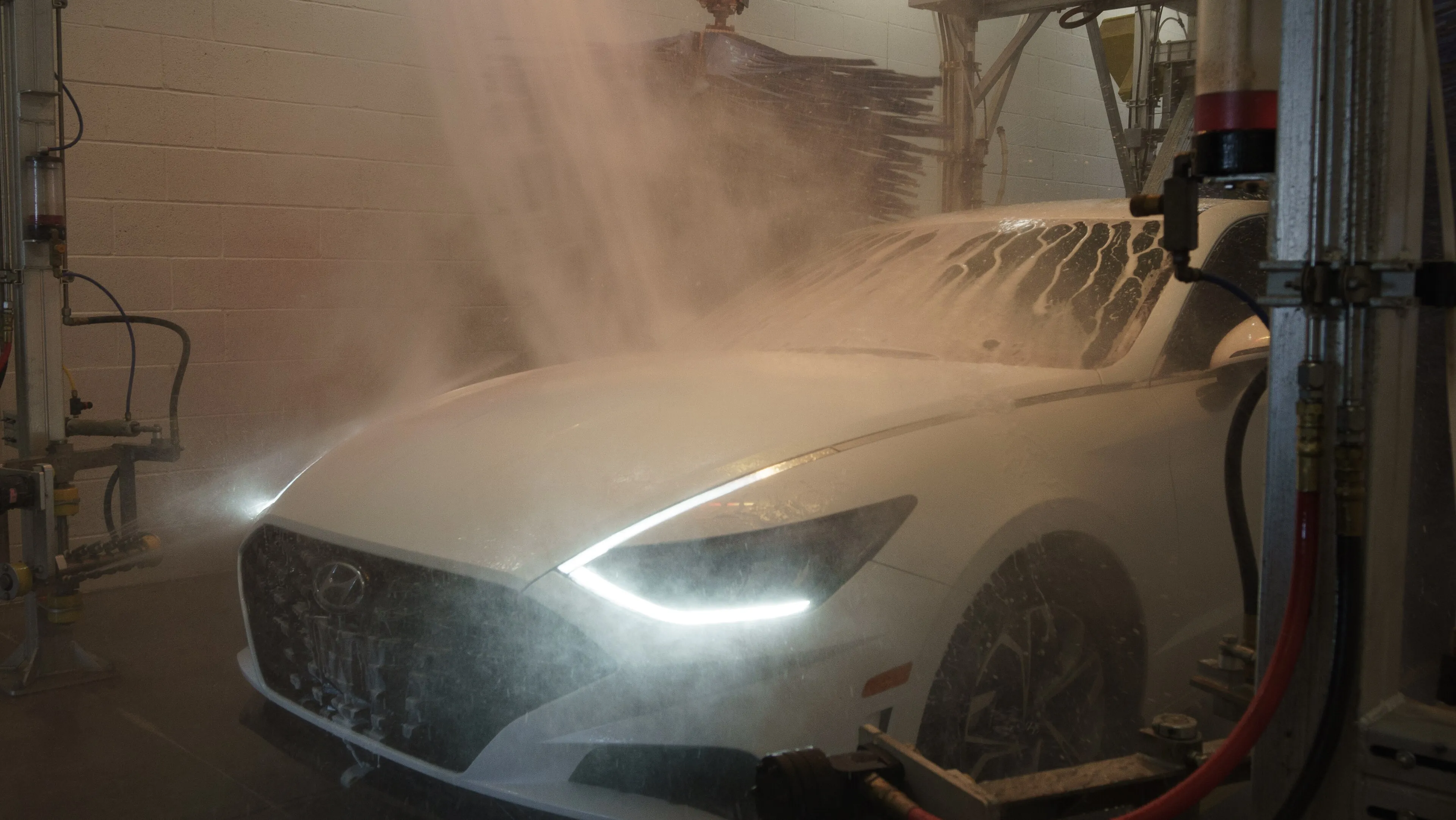 A white car rolling out of a wash bay through mist with its headlights on